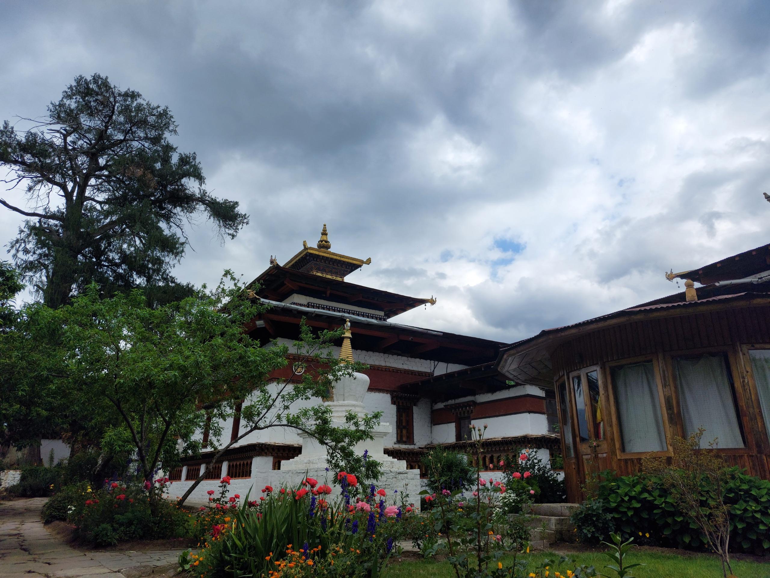 Kyichu Lhakhang framed by flowers and a cloud-filled sky